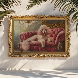 May include: A framed painting featuring a light pink poodle lounging on a tufted, red velvet sofa. The dog wears a gold collar and is set against a backdrop of a chandelier and ornate gold frame. The artwork has a vintage aesthetic.