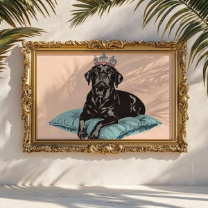 May include: A framed art print featuring a black Labrador Retriever wearing a crown and resting on a teal pillow. The dog is set against a light pink background, framed in an ornate gold frame. The artwork is displayed against a white wall with palm fronds.
