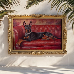May include: A framed portrait of a Doberman Pinscher dog resting on a red leather couch. The dog is black and tan, wearing a jeweled collar. The ornate gold frame adds a touch of elegance to the artwork.