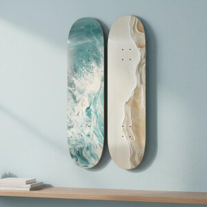 May include: Two skateboard decks mounted vertically. The left deck features a swirling teal, blue, and white abstract pattern resembling ocean waves. The right deck displays a smooth, light beige and cream marbled design with a textured appearance.