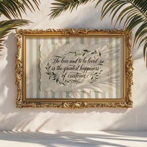 May include: A framed artwork with a gold ornate frame. The artwork features a paper with the quote "To love and to be loved is the greatest happiness of existence" in elegant calligraphy. The background has vertical stripes.