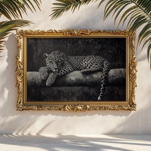 May include: A black and white painting of a leopard resting on a log, framed in an ornate gold frame. The leopard has black spots and is lying down with its paws crossed. The background is dark and the painting is displayed on a white wall.