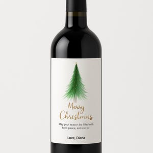 May include: A black wine bottle with a white label featuring a green Christmas tree illustration and the words "Merry Christmas" in gold script. The text "May your season be filled with love, peace, and elet or. Love, Diana" is also on the label.