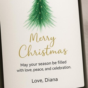 May include: A wine bottle label with a watercolor Christmas tree design. The label features the words "Merry Christmas" in gold script, along with a holiday message and the name "Diana".