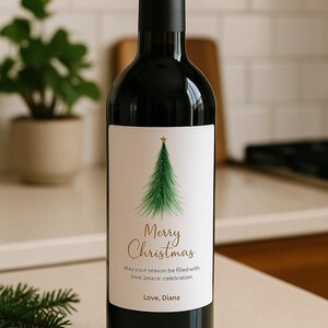 May include: A dark wine bottle with a label featuring a green Christmas tree and the words "Merry Christmas." The label also includes the text "May your season be filled with love; peace: celebration. Love, Diana."