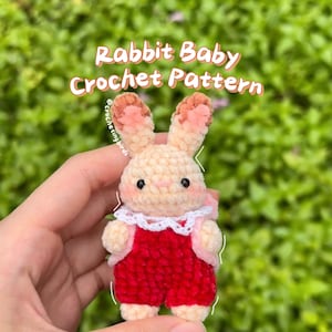 Puede incluir: Un bebé conejo amigurumi de crochet que lleva un mono rojo y un cuello de encaje blanco. El conejo tiene orejas rosas y un cuerpo de color crema. El texto "Rabbit Baby Crochet Pattern" es visible en la parte superior de la imagen.