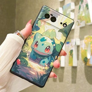 May include: A green and blue Pokemon character, Bulbasaur, is featured on a black phone case. The case has a green and white floral design. The phone case is designed for a Google Pixel phone.