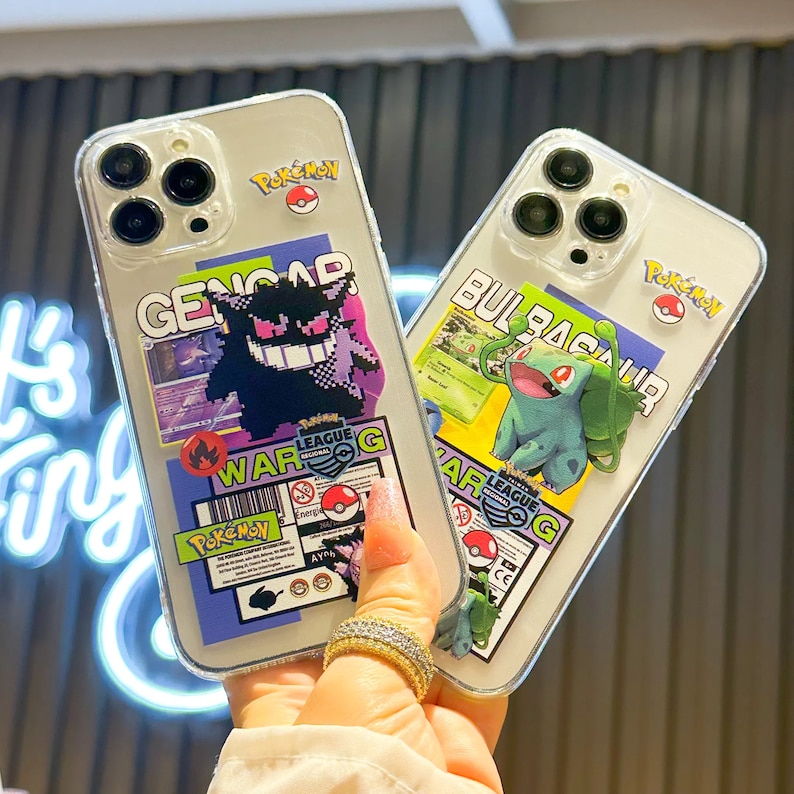 Może przedstawiać: Dwa przezroczyste etui na telefon z kolorowymi wzorami postaci Pokemon. Etui po lewej stronie przedstawia fioletową i czarną postać Genga z tekstem "WAR G" i "Pokemon". Etui po prawej stronie przedstawia zieloną postać Bulbasaura z tekstem "WAR G" i "Pokemon".