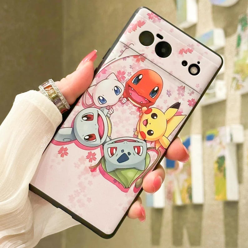 May include: Pink phone case with a design of five cartoon Pokemon characters, including Pikachu, Bulbasaur, Charmander, Squirtle, and Eevee. The case has a floral pattern and a black border.