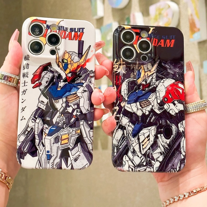 Puede incluir: Dos fundas para tel&eacute;fono con un dise&ntilde;o de robot y el texto "Mobile Suit Gundam". Las fundas son negras y blancas con un dise&ntilde;o de robot colorido.