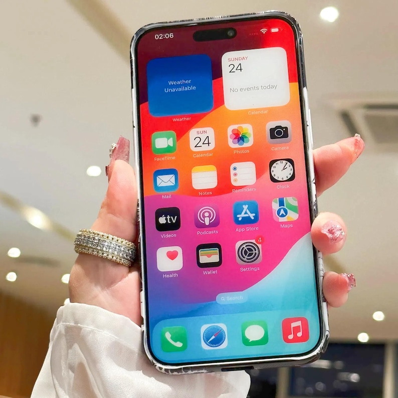Może przedstawiać: Biały iPhone z czarnym ekranem wyświetlającym ekran gł&oacute;wny z r&oacute;żnymi aplikacjami, w tym FaceTime, Kalendarz, Zdjęcia, Poczta, Notatki, Przypomnienia, Zegar, Filmy, Podcasty, App Store, Mapy, Zdrowie, Portfel i Ustawienia. Godzina to 02:06, a data to niedziela, 24.