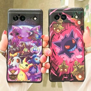 以下が含まれることがあります： 異なるポケモンのデザインが施された黒い携帯電話ケース2つ。最初のケースは、白地に紫と黒のゲンガーが描かれている。2つ目のケースは、赤地にピンクと黒のゲンガーが描かれている。