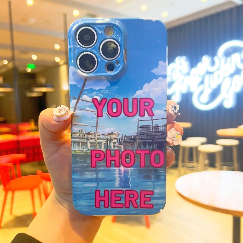 May include: A blue and white phone case with a cityscape and water reflection. The case has the text "YOUR PHOTO HERE" in pink.
