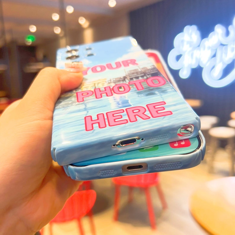 May include: Two phone cases stacked on top of each other. The top case is blue with a white and blue image and the text "YOUR PHOTO HERE" in pink. The bottom case is blue with a white design.