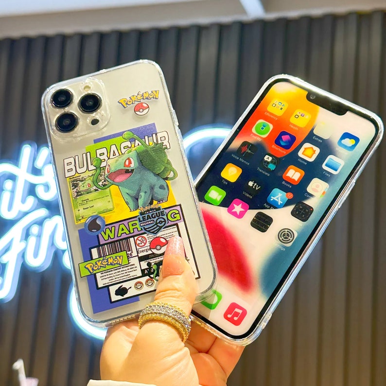 Może przedstawiać: Przezroczyste etui na telefon z motywem Pokemon Bulbasaur. Etui ma kolorystykę niebiesko-zielono-czerwoną na białym tle. Etui ma r&oacute;wnież kod kreskowy i napis "Pokemon" na nim.