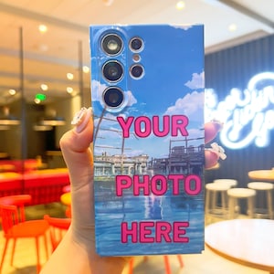 May include: A blue and white phone case with a photo of a cityscape and the text "YOUR PHOTO HERE" in pink.