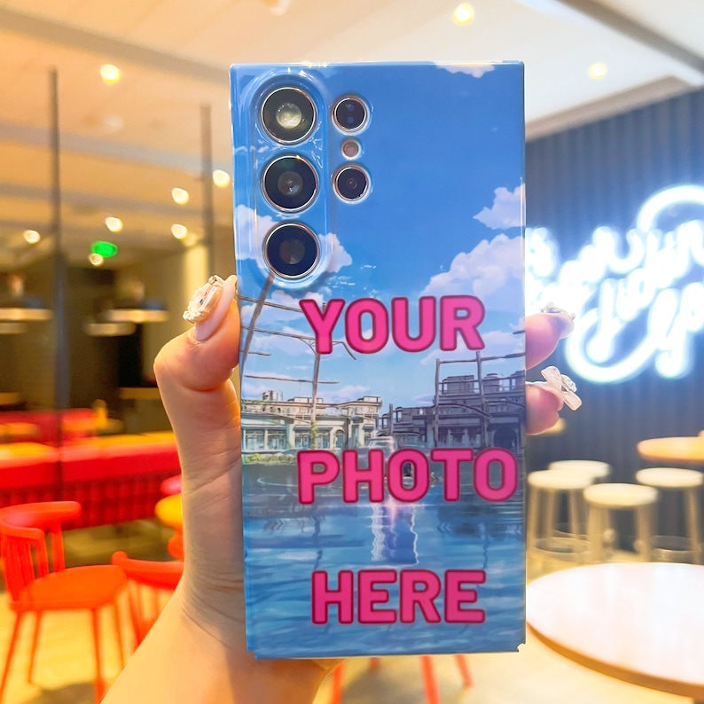 May include: A blue and white phone case with a photo of a cityscape and the text "YOUR PHOTO HERE" in pink.