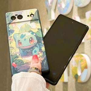 May include: A black phone case with a green cartoon character on the back. The character is a green lizard with red eyes and a white belly. The case is designed to fit a Google Pixel phone.