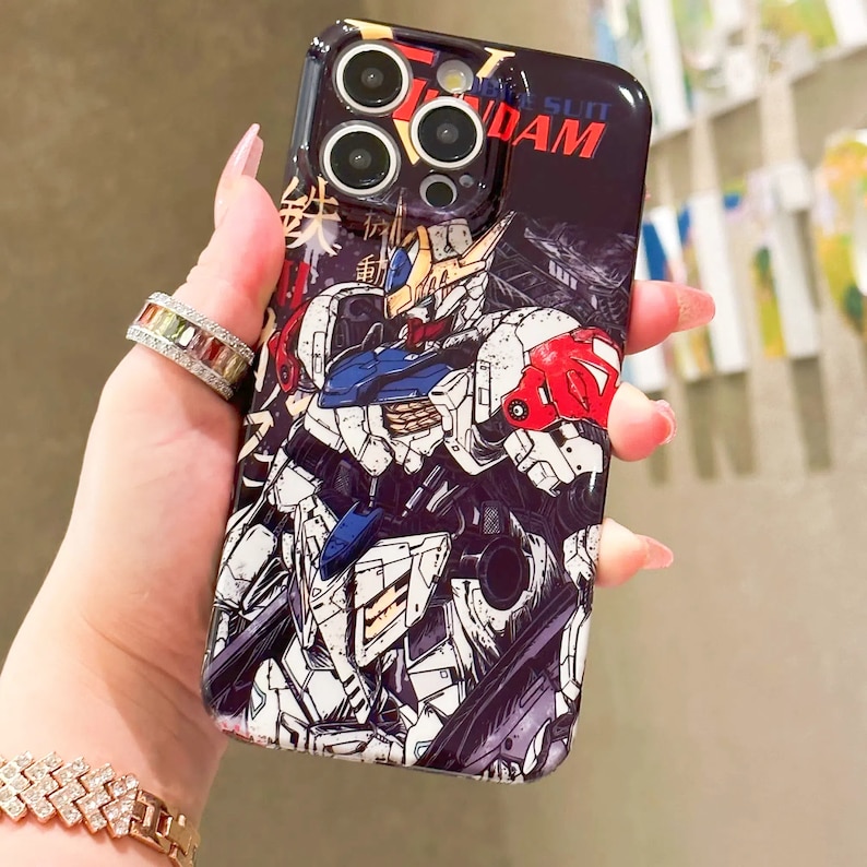 Puede incluir: Una funda de tel&eacute;fono negra con una ilustraci&oacute;n colorida de un robot con el texto "Mobile Suit Gundam" en la funda.