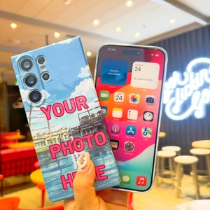 May include: A blue and white phone case with a cartoon image of a cityscape and the text "YOUR PHOTO HERE". The case is being held in a hand with painted nails.