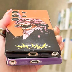 Może przedstawiać: Czarne etui na telefon z pomarańczowym tłem i grafiką postaci z anime Evangelion. Etui ma czarny i ż&oacute;łty napis "EVANGELION".
