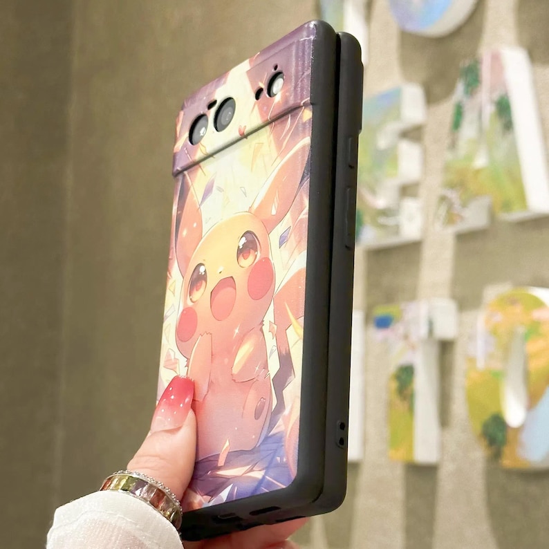 May include: A black phone case with a colorful illustration of Pikachu, a popular Pokemon character, on the back. The case has a raised camera bump and a black border.