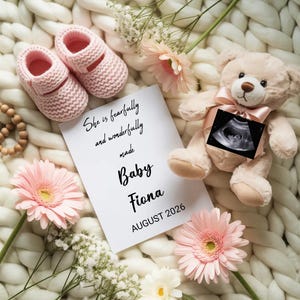 May include: A baby announcement featuring pink baby booties, a teddy bear with a sonogram, and a card that reads "She is fearfully and wonderfully made Baby Fiona AUGUST 2026". The scene is decorated with pink flowers and white flowers.