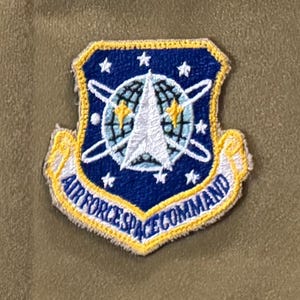 May include: A blue and white embroidered patch with a globe and a star in the center. The text "AIR FORCE SPACE COMMAND" is written in a yellow arc around the globe.