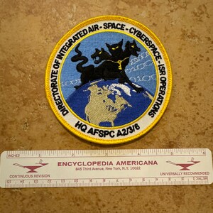 May include: A yellow and blue embroidered patch with a black three-headed dog, a globe, and the text "Directorate of Integrated Air-Space-Cyberspace-ISR Operations HQ AFSPC A2/3/6".