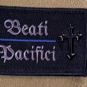 May include: Black embroidered patch with a blue line and the text "Beati Pacifici" in white. A silver cross is on the right side of the patch.