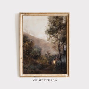 May include: A framed landscape painting depicts a cabin nestled in a forest, with a path leading to it. The artwork features a muted color palette of browns, greens, and beige, with a soft, hazy atmosphere. The frame is a light, distressed wood.