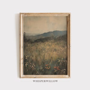 May include: A framed painting depicting a landscape scene with a field of wildflowers in the foreground and a mountain range in the background. The sky is a soft blue with hints of pink and orange.