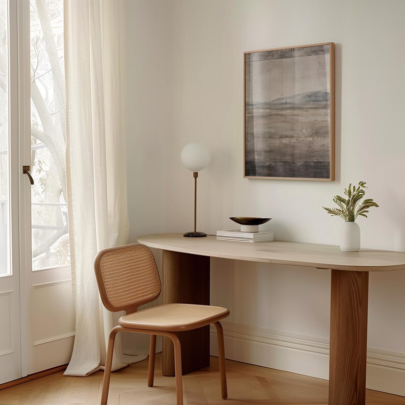 K&ouml;nnte beinhalten: Ein heller Holzschreibtisch mit abgerundeter Kante, eine braune Metalllampe mit wei&szlig;er Kugel und ein gerahmtes Landschaftskunstwerk. Ein Stuhl mit Flechtwerk und eine wei&szlig;e Vase mit Gr&uuml;n sind ebenfalls zu sehen.