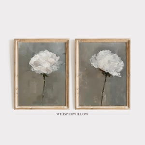 May include: Two framed paintings of white flowers on a gray background. The paintings are in simple gold frames.