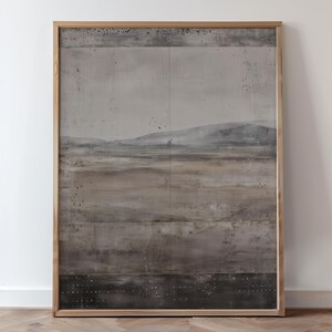 K&ouml;nnte beinhalten: Abstrakte Landschaftsmalerei in einem hellen Holzrahmen. Das Kunstwerk zeigt eine ged&auml;mpfte Farbpalette aus Grau-, Braun- und Schwarzt&ouml;nen mit strukturiertem Aussehen. Die Komposition umfasst eine Horizontlinie und eine Andeutung von Bergen.
