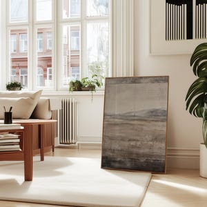 K&ouml;nnte beinhalten: Ein helles Wohnzimmer mit einem cremefarbenen Sofa, einem Couchtisch aus Holz und einem gro&szlig;en gerahmten Landschaftsbild. Eine Topfpflanze mit gro&szlig;en gr&uuml;nen Bl&auml;ttern steht in der N&auml;he des Gem&auml;ldes. Der Raum hat gro&szlig;e Fenster und einen hellen Teppich.