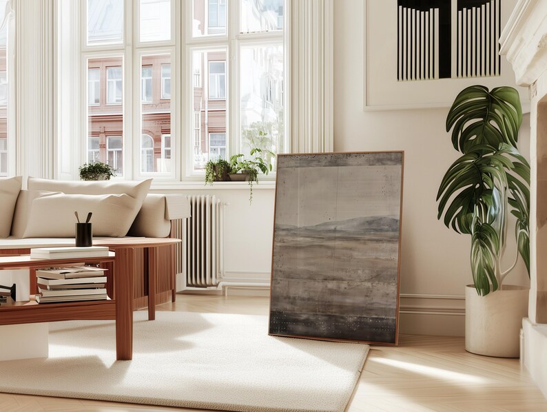 K&ouml;nnte beinhalten: Ein helles Wohnzimmer mit einem cremefarbenen Sofa, einem Couchtisch aus Holz und einem gro&szlig;en gerahmten Landschaftsbild. Eine Topfpflanze mit gro&szlig;en gr&uuml;nen Bl&auml;ttern steht in der N&auml;he des Gem&auml;ldes. Der Raum hat gro&szlig;e Fenster und einen hellen Teppich.