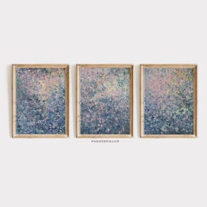 May include: Three framed abstract paintings with a blue, purple, and pink colour scheme. The paintings are in a light wood frame and have a textured, abstract design.