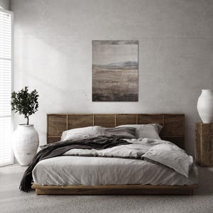K&ouml;nnte beinhalten: Ein Schlafzimmer mit einem Bett mit Holzrahmen und einem gewebten Kopfteil. Das Bett ist mit hellgrauer Bettw&auml;sche und einer dunkelgrauen Decke bedeckt. &Uuml;ber dem Bett h&auml;ngt ein Landschaftsbild, und eine gro&szlig;e wei&szlig;e Vase steht auf einem Holzblock.
