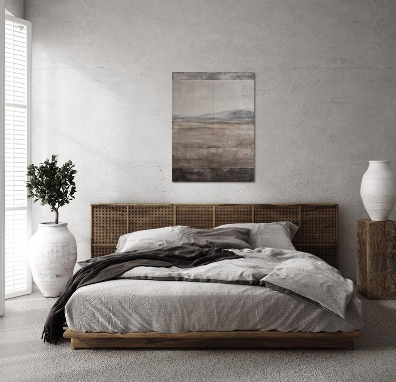 K&ouml;nnte beinhalten: Ein Schlafzimmer mit einem Bett mit Holzrahmen und einem gewebten Kopfteil. Das Bett ist mit hellgrauer Bettw&auml;sche und einer dunkelgrauen Decke bedeckt. &Uuml;ber dem Bett h&auml;ngt ein Landschaftsbild, und eine gro&szlig;e wei&szlig;e Vase steht auf einem Holzblock.