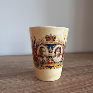 Może przedstawiać: Kremowy ceramiczny kubek z pamiątkowym wzorem z okazji koronacji 12 maja 1937 roku. Przedstawia portrety króla Jerzego VI i królowej Elżbiety, koronę, flagi oraz napis 12th May 1937 i CORONATION.