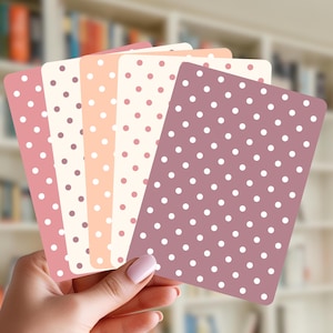 May include: A set of five rectangular cards with rounded corners, each featuring a different solid background color including mauve, cream, peach, and light pink, all decorated with a repeating pattern of small, evenly spaced white polka dots.