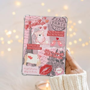 May include: A pink and clear case featuring a collage design with a teddy bear, Eiffel Tower, hearts, and text. The text includes phrases like "Buy Me Books and Tell Me I'm Pretty" and "Books are my Love Language."