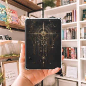 Può includere: Una custodia per telefono nera con un design geometrico dorato con una stella e forme pendenti. Il design è su uno sfondo scuro con un effetto galassia sottile.