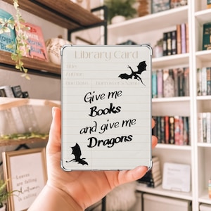 Peut inclure: Une carte de bibliothèque blanche avec une silhouette de dragon noir et le texte "Give me Books and give me Dragons".