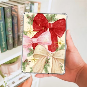 May include: A rectangular tablet case featuring a festive illustration of three large bows in red, light pink, and cream colours. The design includes green pine needle sprigs, small red berries, and gold starburst accents on a cream background.
