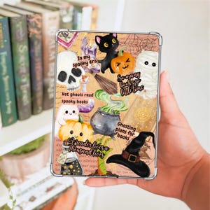 May include: A clear tablet case featuring a collage of Halloween-themed illustrations including a black cat, a pumpkin, a skull, a mummy, a witch hat, and a cauldron with green smoke, alongside text reading In my spooky era and A reader lives a thousand lives.