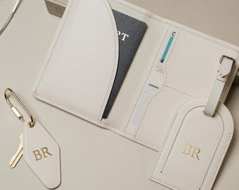 May include: An off-white passport holder with interior card slots, a matching luggage tag, and a hotel-style keychain, all featuring the gold-embossed initials BR. The passport holder contains a dark blue passport and white cards.