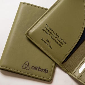 May include: Olive green leather passport holder with the Airbnb logo and a quote: "The world is a book, and those who do not travel read only one page." Includes a passport and cash. The date "November 2025" is also visible.