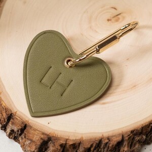 Puede incluir: Llavero en forma de coraz&oacute;n verde oliva con herrajes dorados. El llavero presenta las iniciales "LH" en relieve en la parte delantera. El clip est&aacute; sujeto a la parte superior del coraz&oacute;n.